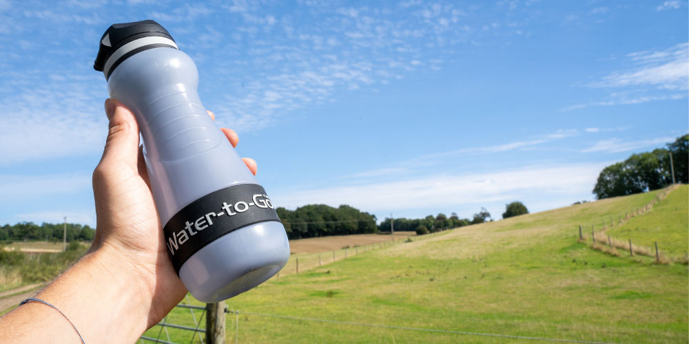 small water filtration bottle held in hand with pasture in background